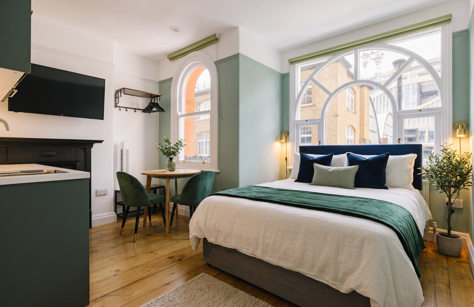After: the same flat with a navy headboard, green velvet chairs and brass wall lights