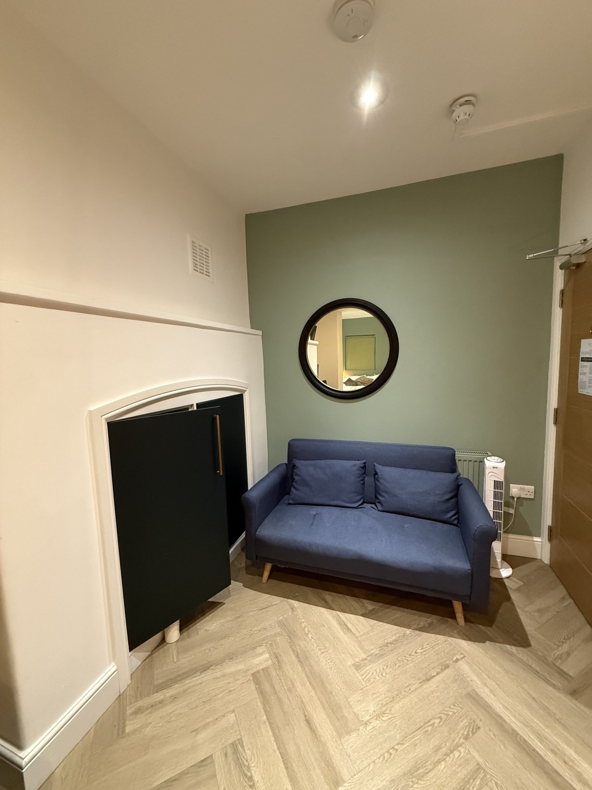 Before: a worn blue sofa, a round mirror and a tower fan