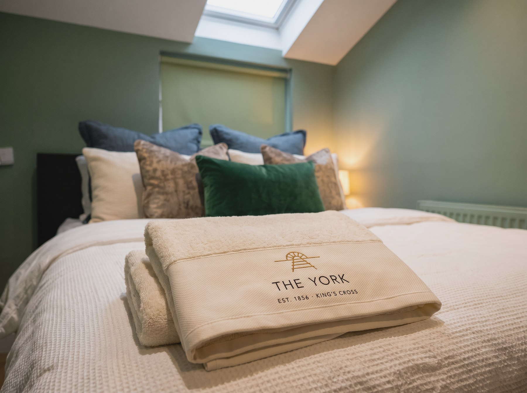 A cream bed with a folded towel carrying The York's embroidered mark
