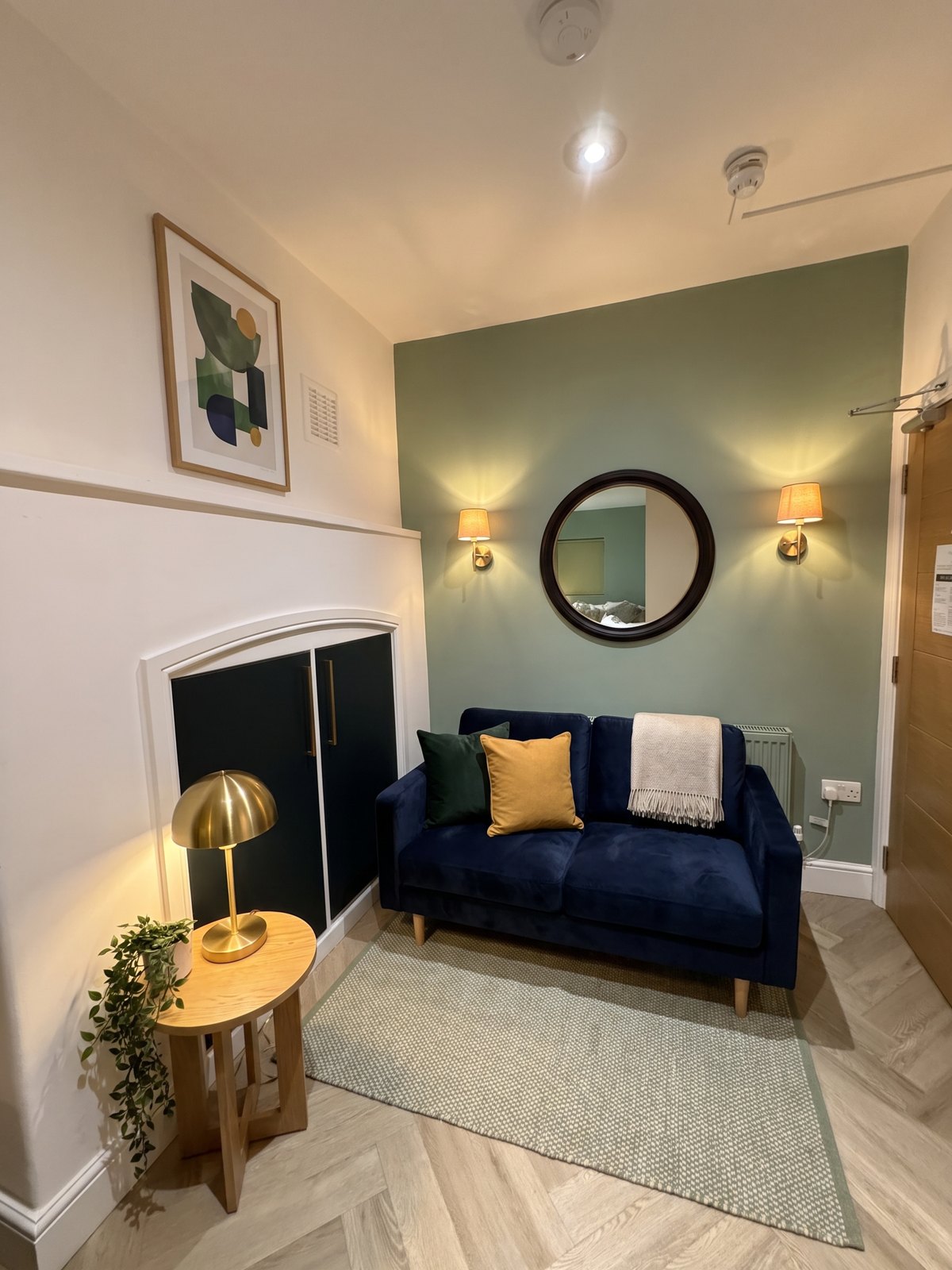 After: a navy velvet sofa, brass wall lights, a rug and one framed print